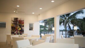 Un restaurante moderno con mobiliario blanco, ventanas amplias y vistas a palmeras.