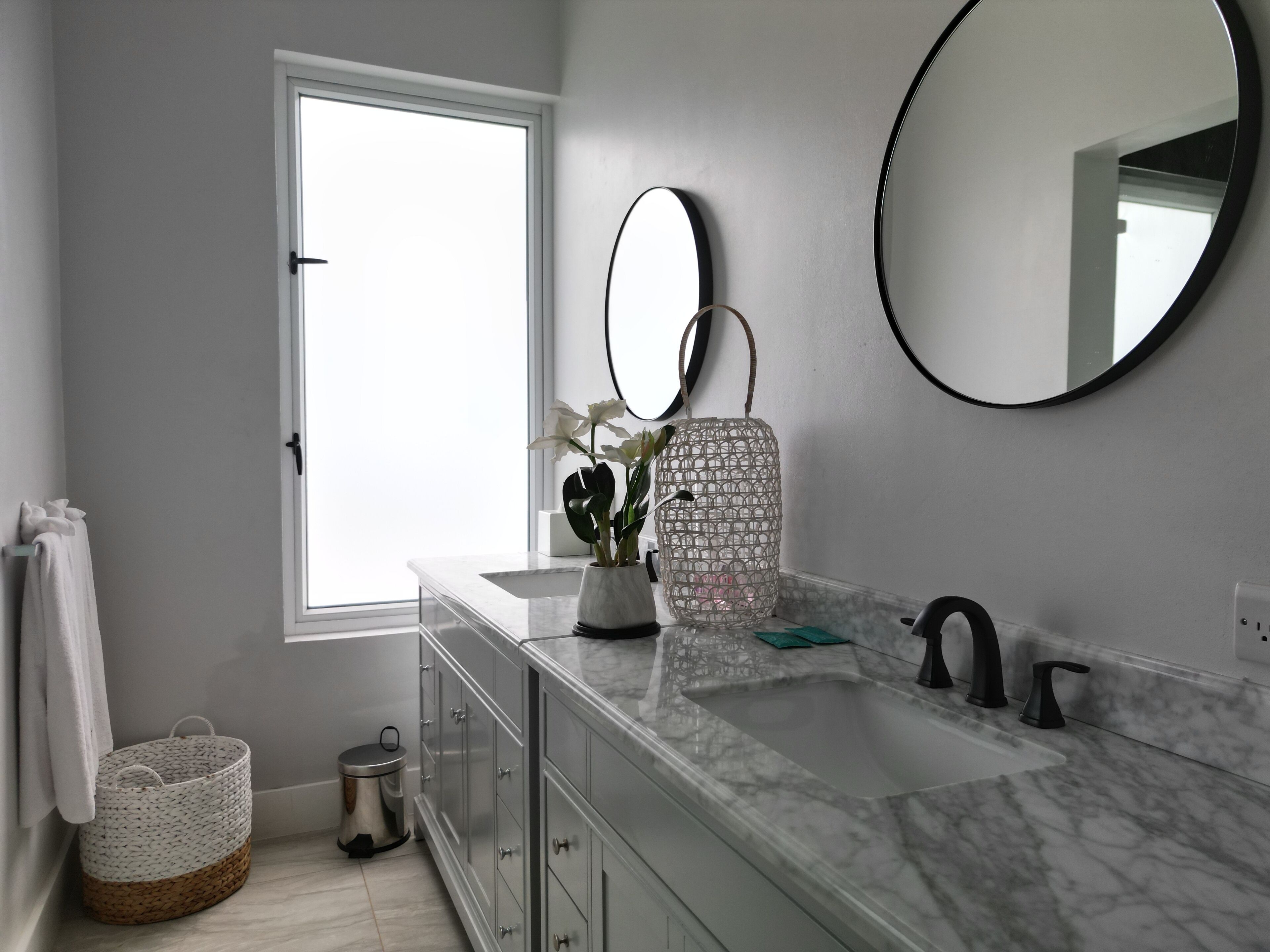 Une salle de bain moderne avec une grande fenêtre, un lavabo en marbre, un miroir rond et une plante en pot.