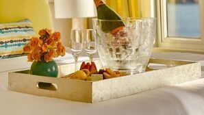 Una bandeja de desayuno ordenada con una botella de champán, copas con hielo, un florero con flores y una caja de frutas variadas sobre una cama.