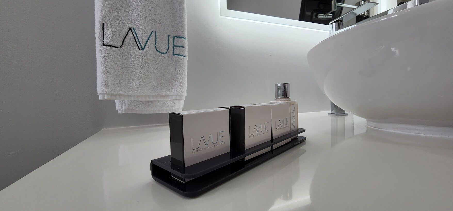 A bathroom with a white sink, a large mirror, and a towel hanging on the wall with the word "LAVUE" embroidered on it.