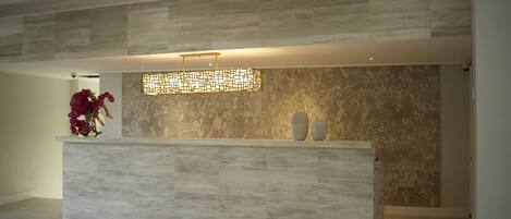 A reception area with a modern design, featuring a marble wall and a light-colored reception desk.