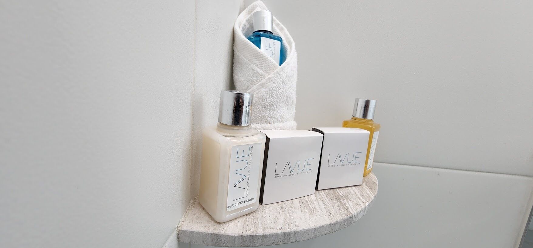 A bathroom shelf with three LAVUE hair conditioner bottles and a white towel.