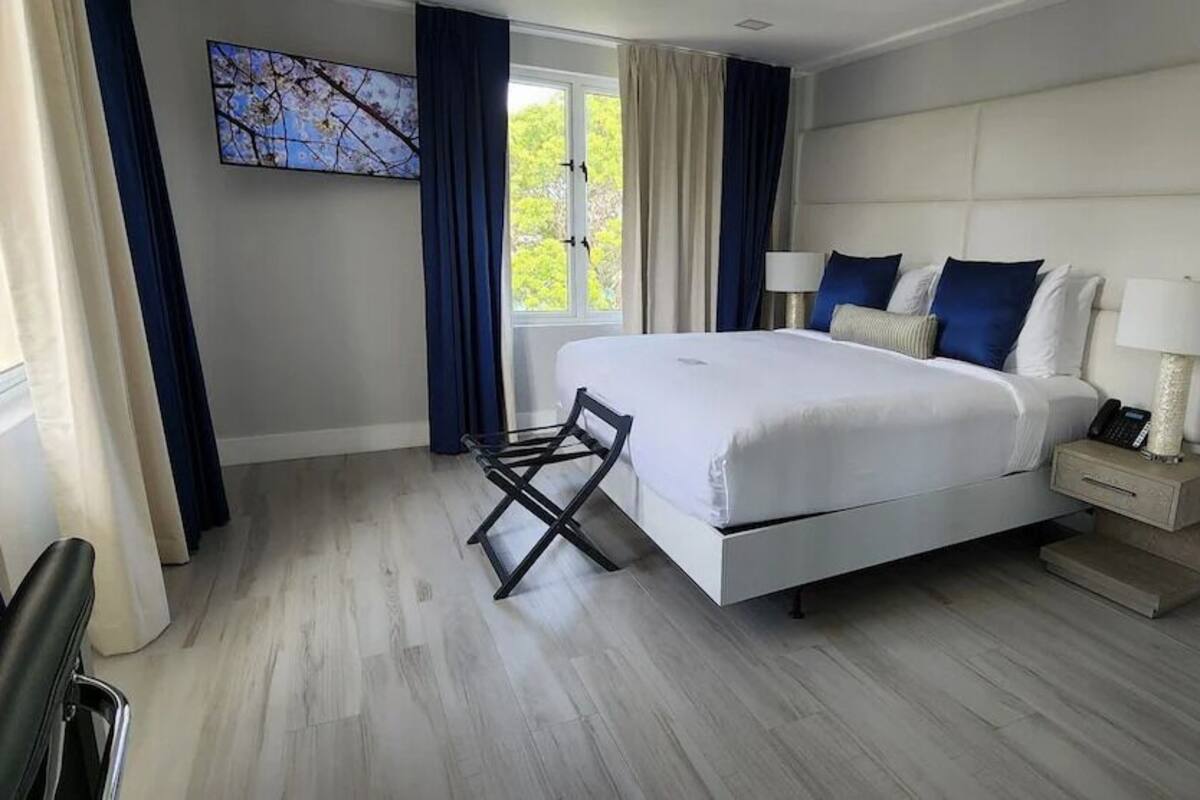 Una habitación de hotel moderna con una cama grande, una mesita de noche con lámpara y vistas al exterior.