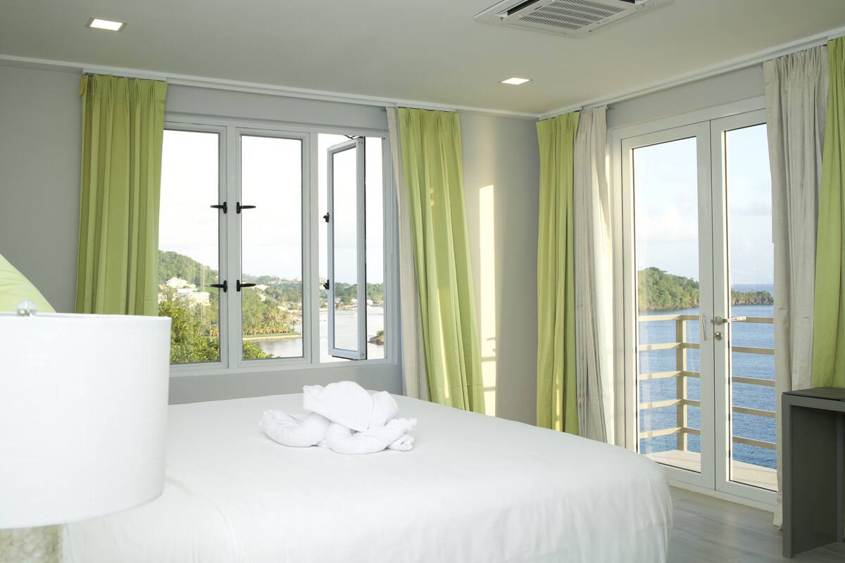 Habitación de hotel con cama, ventana con cortinas y vista hacia el agua.