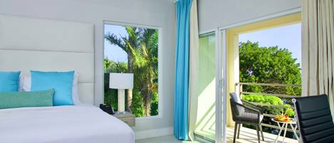 Een hotelkamer met een bed, telefoon, lamp, stoel en balkon met uitzicht op groen.