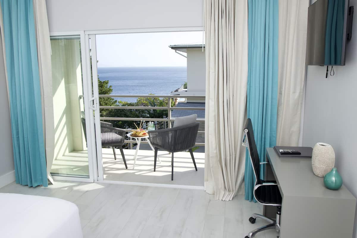 Habitación de hotel con balcón, escritorio, silla y cama.