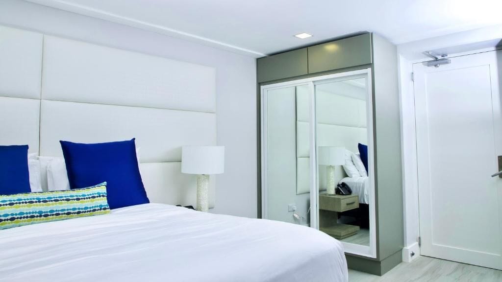 Quarto de hotel com uma cama grande, um guarda-roupa, um espelho e uma porta.
