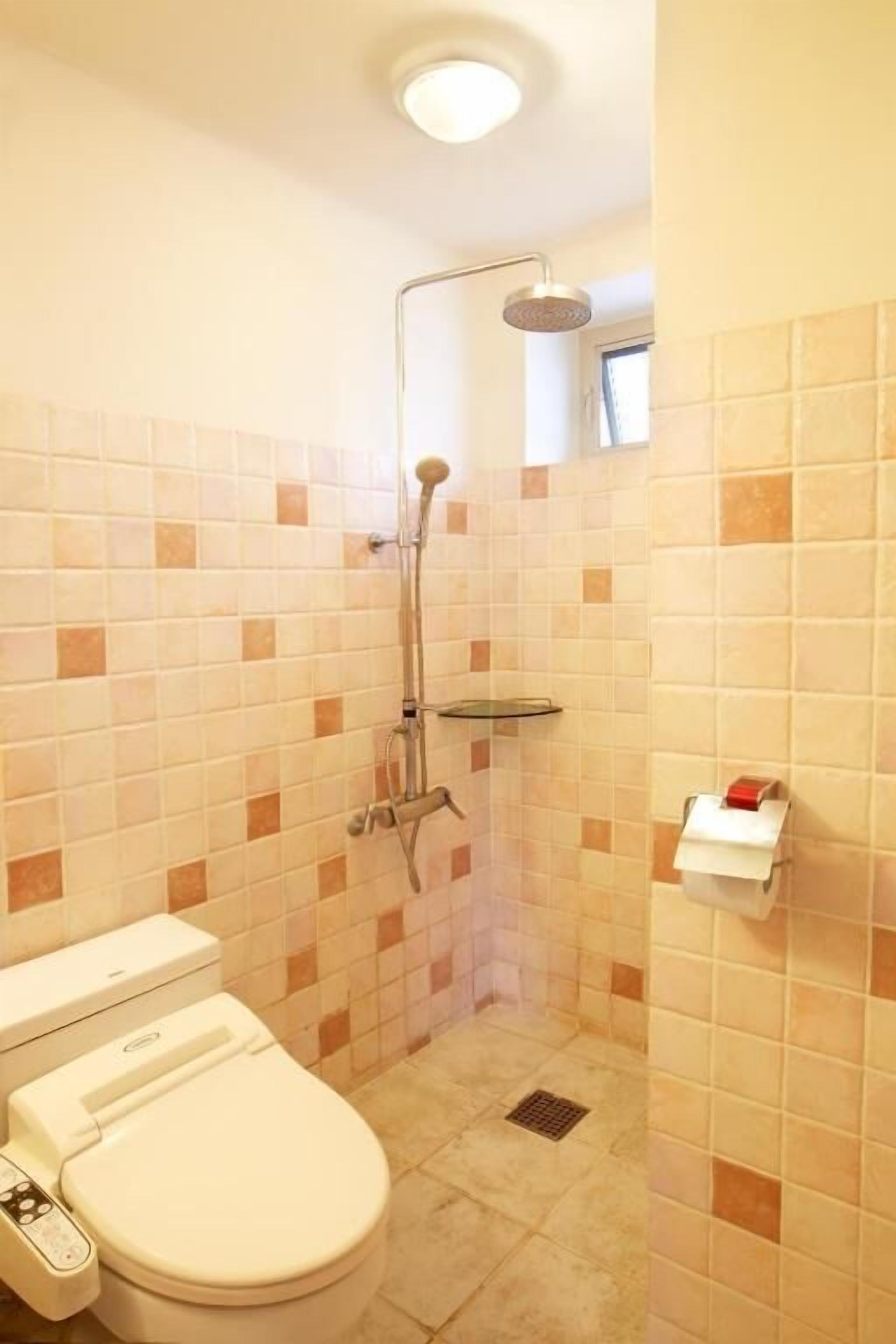 Een badkamer met een toilet, een douche en een betegelde muur.