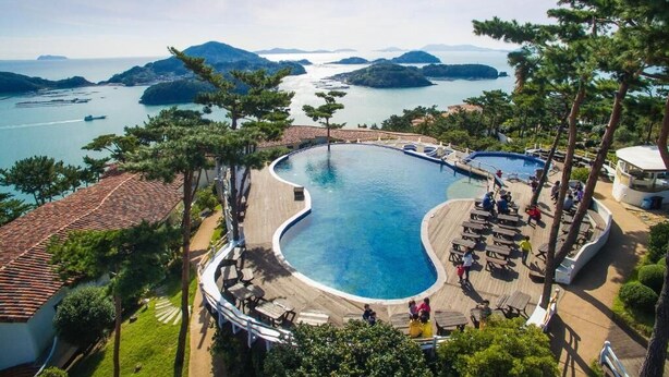 Een resort met een groot, gebogen zwembad, omringd door loungeplekken en uitzicht op zee en eilanden.