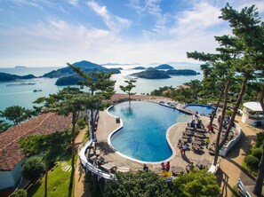 Un resort con una amplia piscina curvada, rodeada de zonas de descanso y vistas al mar y a las islas.