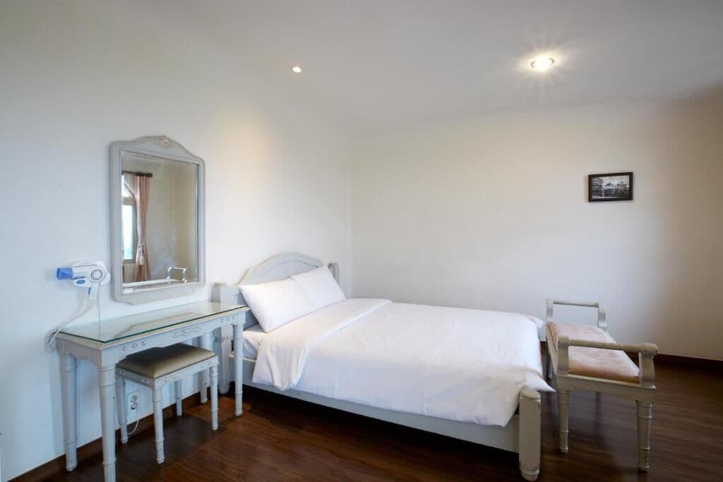 Quarto com cama, mesa de cabeceira, cadeira, espelho e um quadro na parede.
