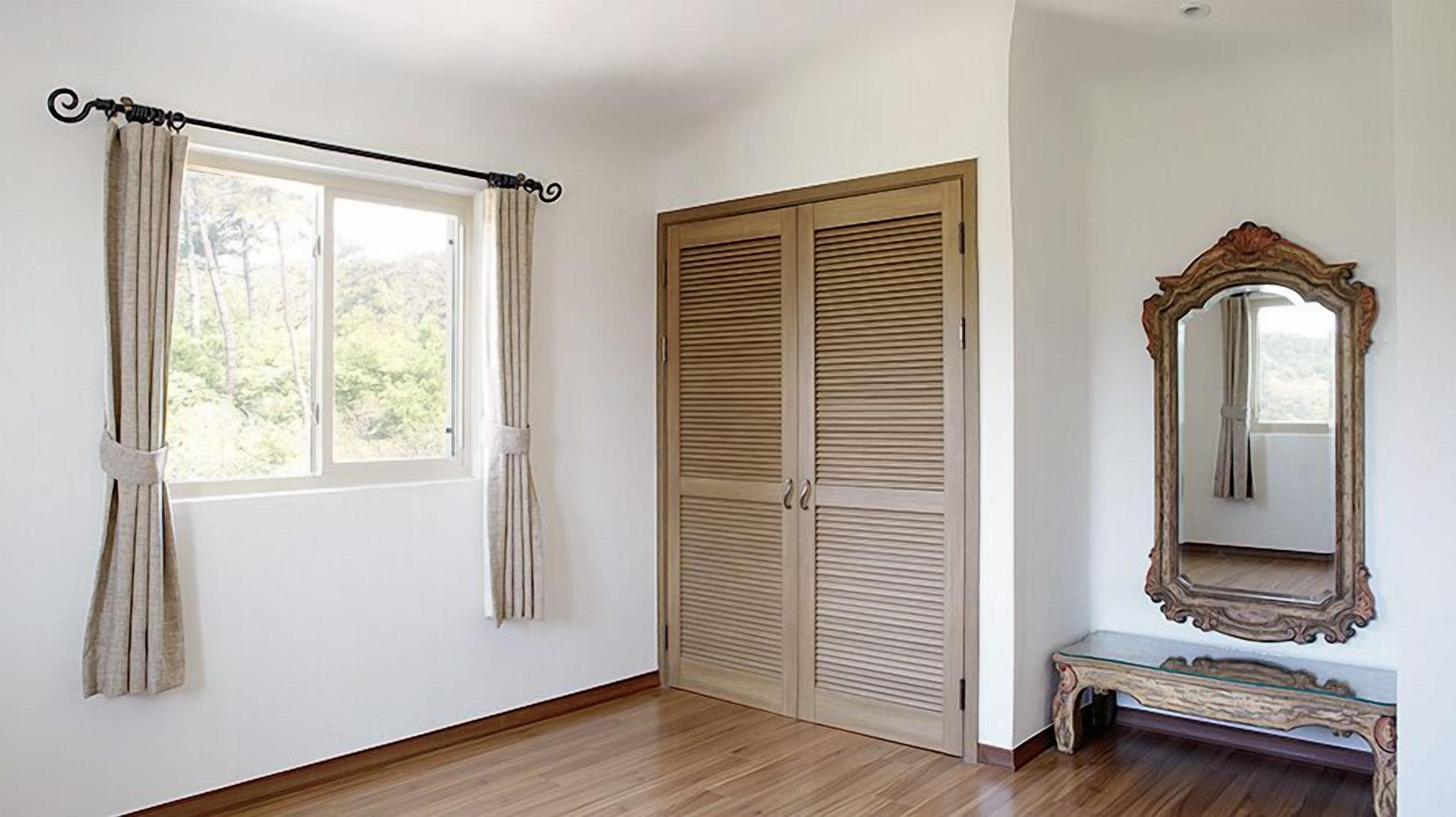 Une pièce avec une grande fenêtre, un plancher en bois, une armoire et un miroir.