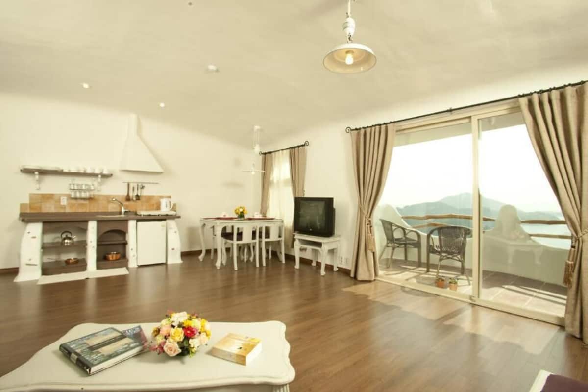 A modern living room with a kitchen, a dining area, and a balcony with a view.