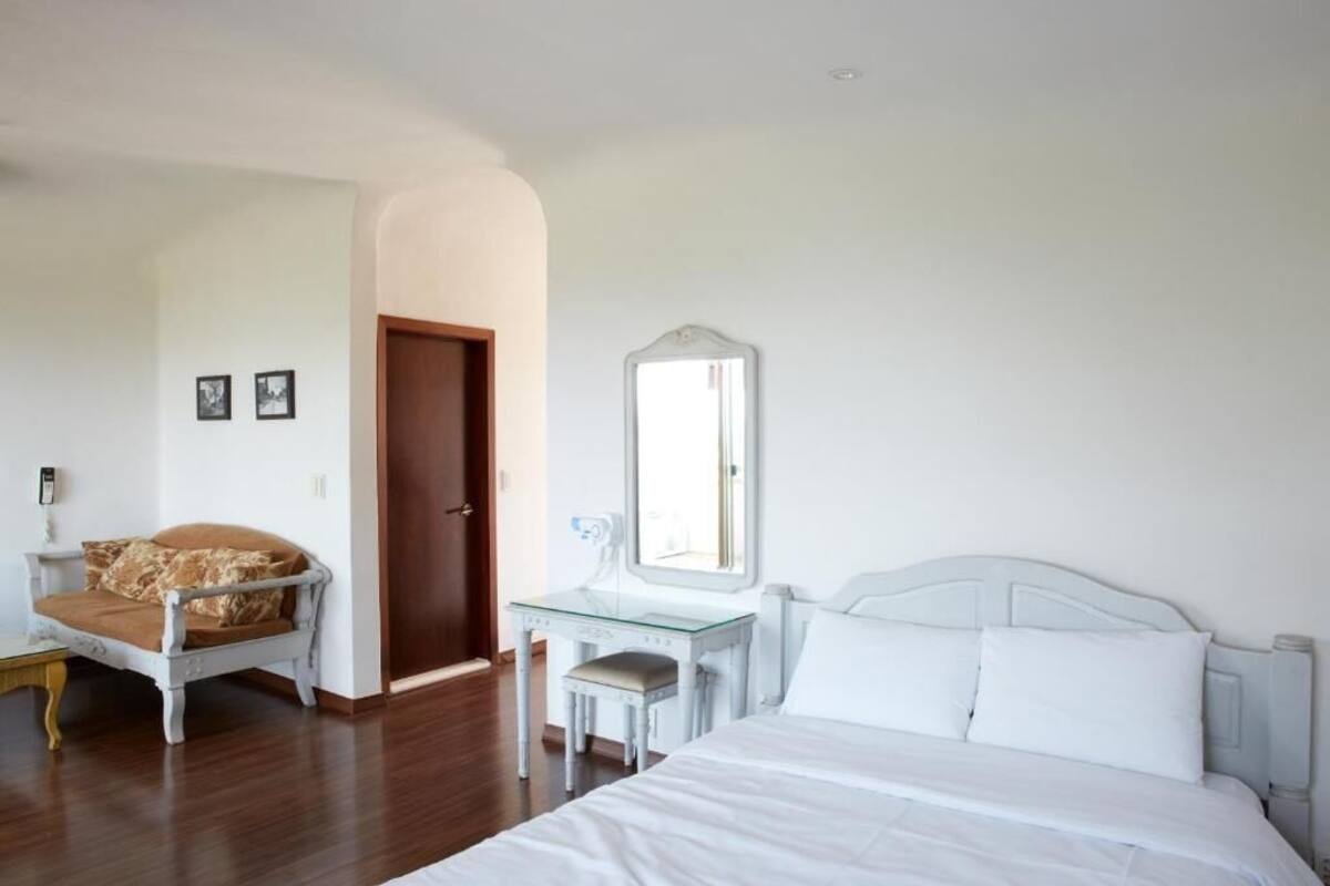 A bedroom with a bed, a desk, a chair, and a mirror.