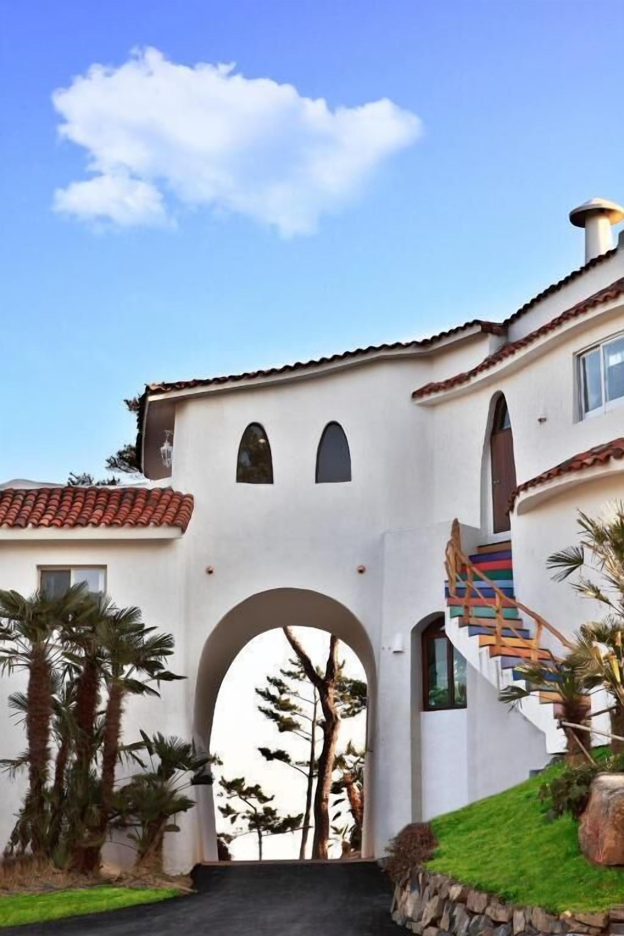 Un edificio de estilo mediterráneo con un arco central, una escalera y palmeras.