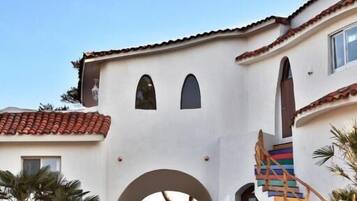 Un edificio de estilo mediterráneo con un arco central, una escalera y palmeras.