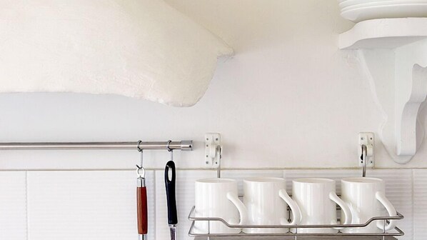 Una cocina con armarios blancos, un estante de acero inoxidable con tazas blancas, y un cuchillo con mango de madera colgado en la pared.