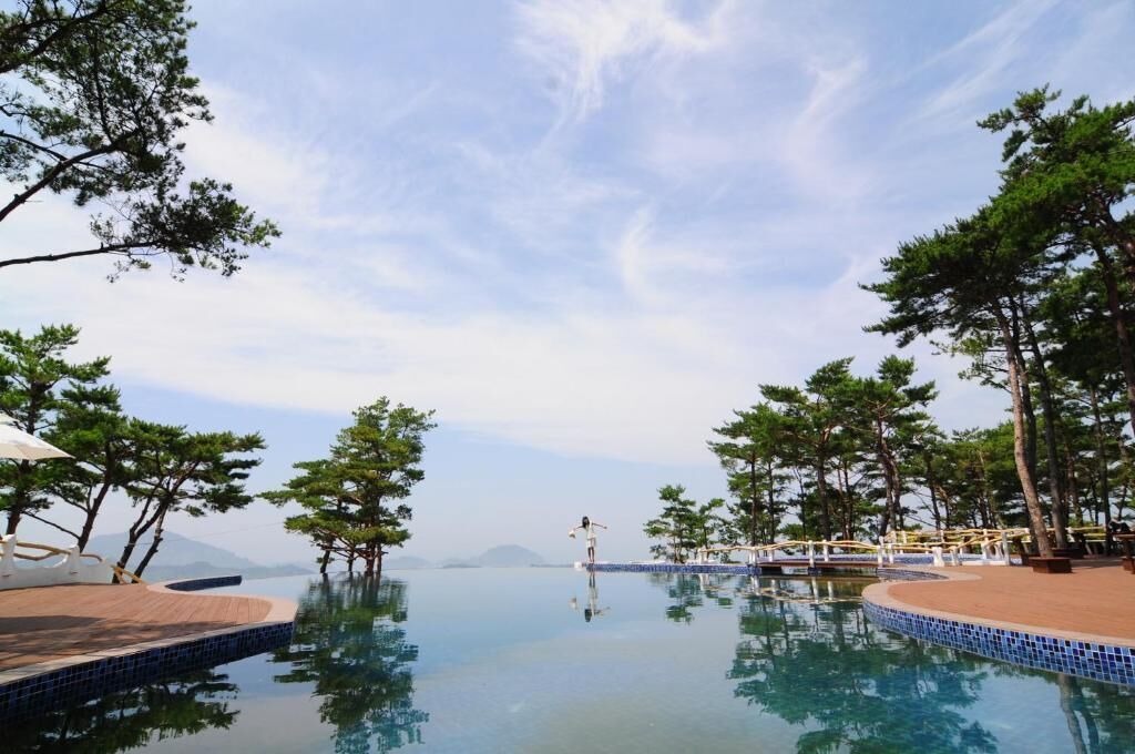A serene infinity pool with clear water, surrounded by trees and a wooden deck.