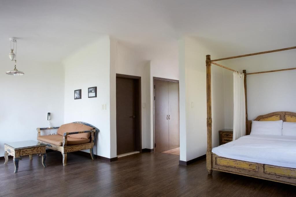 A bedroom with a four-poster bed, a wooden chair, a small table, and a wardrobe.