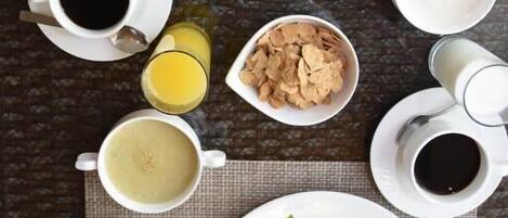 Una mesa con un desayuno abundante que incluye croissants, queso, tomates, lechuga y varios otros alimentos en platos, además de tazas de café y jugo.