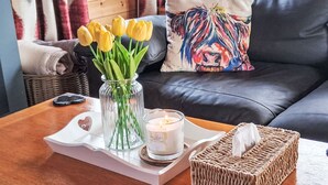 Une table basse en bois sur laquelle se trouve un vase de tulipes jaunes, une bougie allumée et une boîte de mouchoirs.