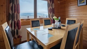 Une pièce aux murs lambrés, avec une grande table et des chaises, une vue par la fenêtre et un luminaire suspendu.