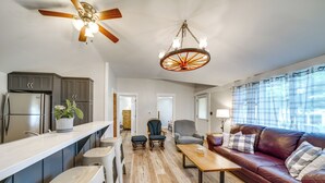 A spacious living area with a wooden floor, a leather sofa, a coffee table, and a kitchen with dark cabinets and a refrigerator. - Walk to Beach & Lake: Idyllic Escape in Edinboro! (Edinboro)