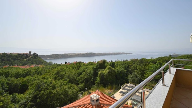 Ein Balkon mit freiem Blick auf eine Küstenlandschaft, einschließlich eines Gewässers und weiter Gebäude in der Ferne.