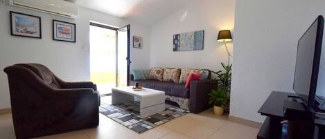 Uma sala de estar com sofá, poltrona, mesa de centro e rack para televisão.
