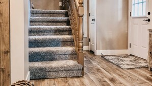 A staircase with carpeted steps and wooden railings, leading to a door with a window.