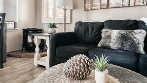 A living room with a dark sofa, a round coffee table with decorative items, a lamp, and a painting on the wall.