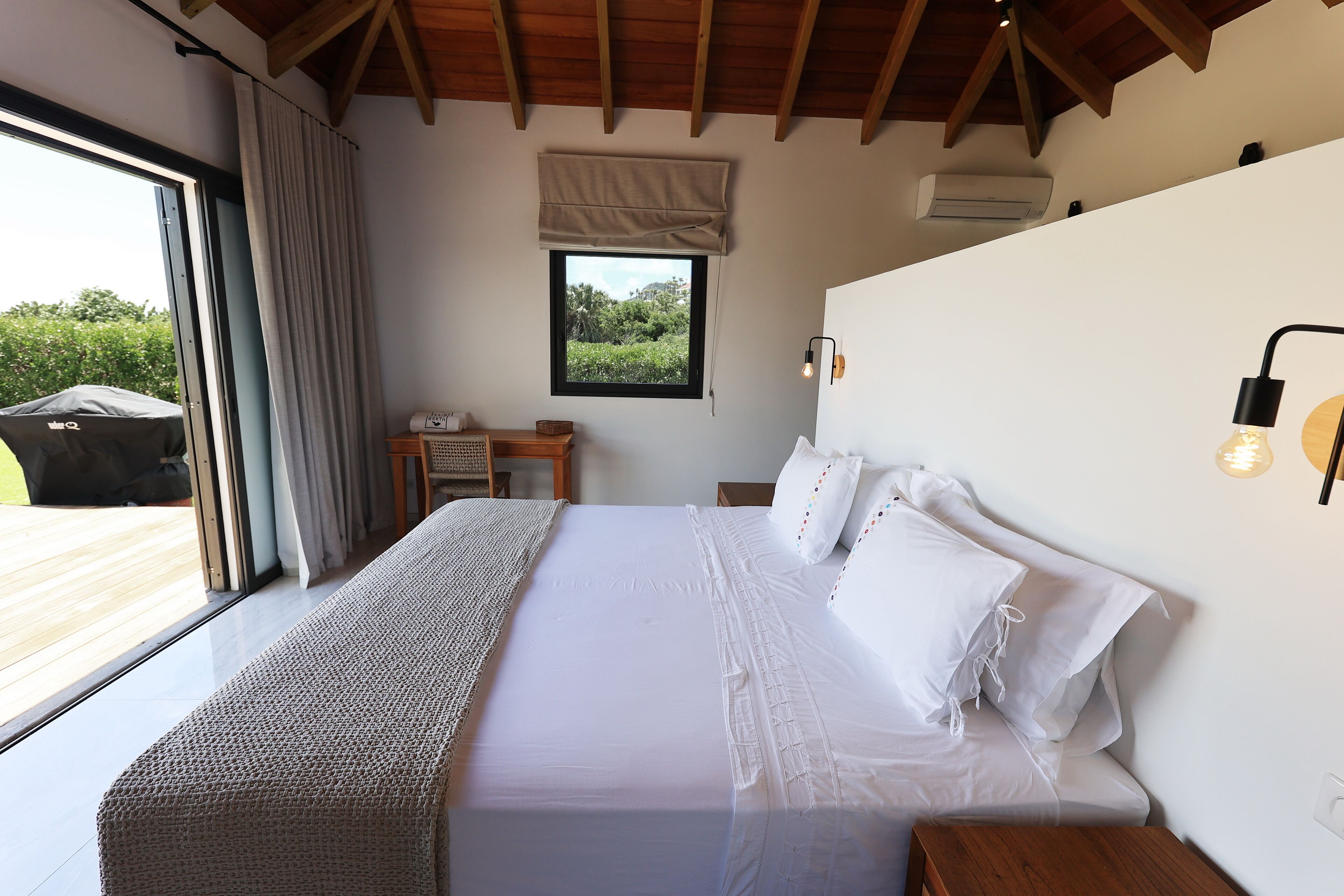 Una camera da letto con un letto grande, una finestra vista su vegetazione, un soffitto in legno e un piccolo tavolo con una lampada.