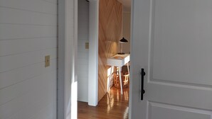 Un pasillo con piso de madera, una puerta blanca con picaporte negro y una pared blanca con puerta corrediza de estilo rústico.
