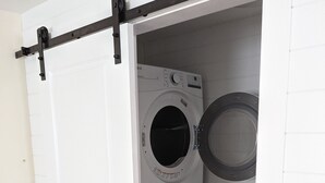 Un lavadero con una puerta blanca, dos lavadoras apiladas y piso de madera.