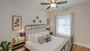 Een slaapkamer met een bed, bedlampen, een plafondventilator en een raam met zonwering.