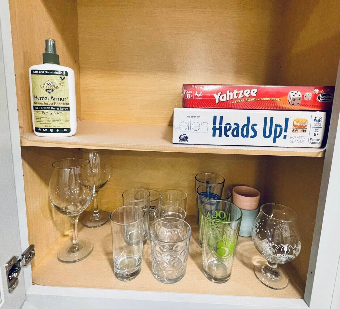 Una estantería con una botella de All Terrain Herbal Armor, un juego de Yahtzee y varios vasos.