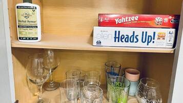 Una estantería con una botella de All Terrain Herbal Armor, un juego de Yahtzee y varios vasos.