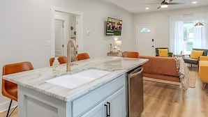 Een moderne keuken met een marmeren aanrecht, een spoelbak en een ingebouwde oven. Er is een eethoek met een tafel en stoelen, en een woonkamer met een bank en salontafel.