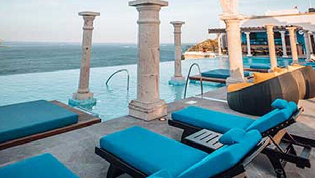 An infinity pool with blue lounge chairs, a stone archway, and a view of the sea. - 3 BR PENTHOUSE AT VISTA ENCANTADA RESORT RANKED #2 IN CABO SAN LUCAS (Cabo San Lucas)