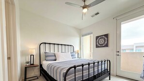 A bedroom with a bed, bedside lamps, a ceiling fan, a window, and a door.