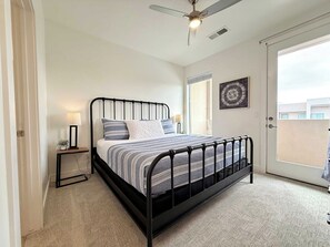 A bedroom with a bed, bedside lamps, a ceiling fan, a window, and a door.