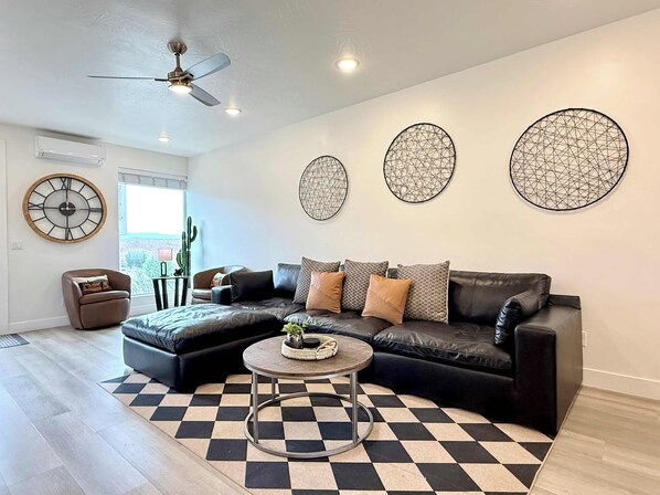 A modern living room with a black leather sectional sofa, a round coffee table, and a checkered floor.