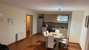 Une cuisine compacte dotée d’appareils électroménagers modernes, un coin repas avec une table et des chaises en bois, et un radiateur apparent.