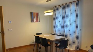 Un coin repas avec une table en bois et des chaises noires, un tableau au mur et un rideau à motifs.