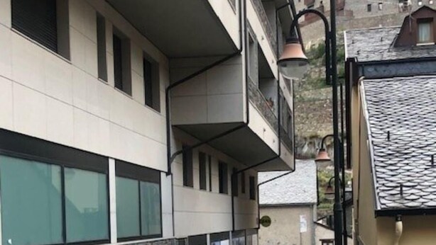 Un étroit chemin piétonnier bordé d’un côté par une rangée de jardinières et de l’autre par un immeuble doté d’un balcon.
