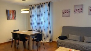 Un salon moderne comprenant une table à manger, des chaises, un canapé et une petite table ornée d’un vase de fleurs.
