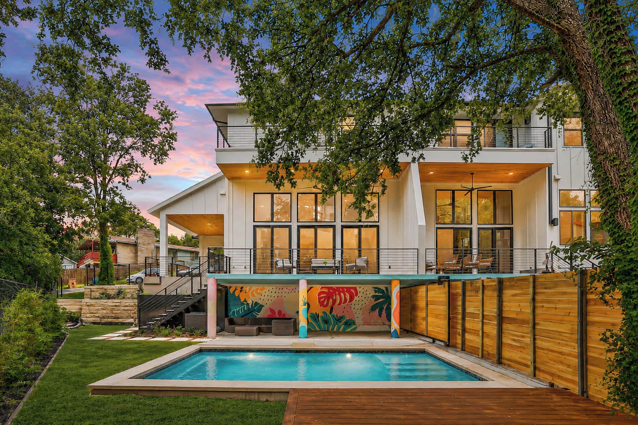 A modern two-story house with a swimming pool, large windows, and a wooden deck.