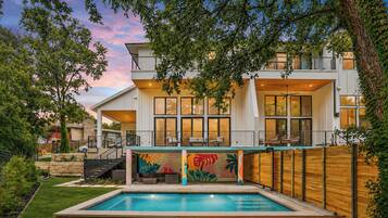 A modern two-story house with a swimming pool, large windows, and a wooden deck.