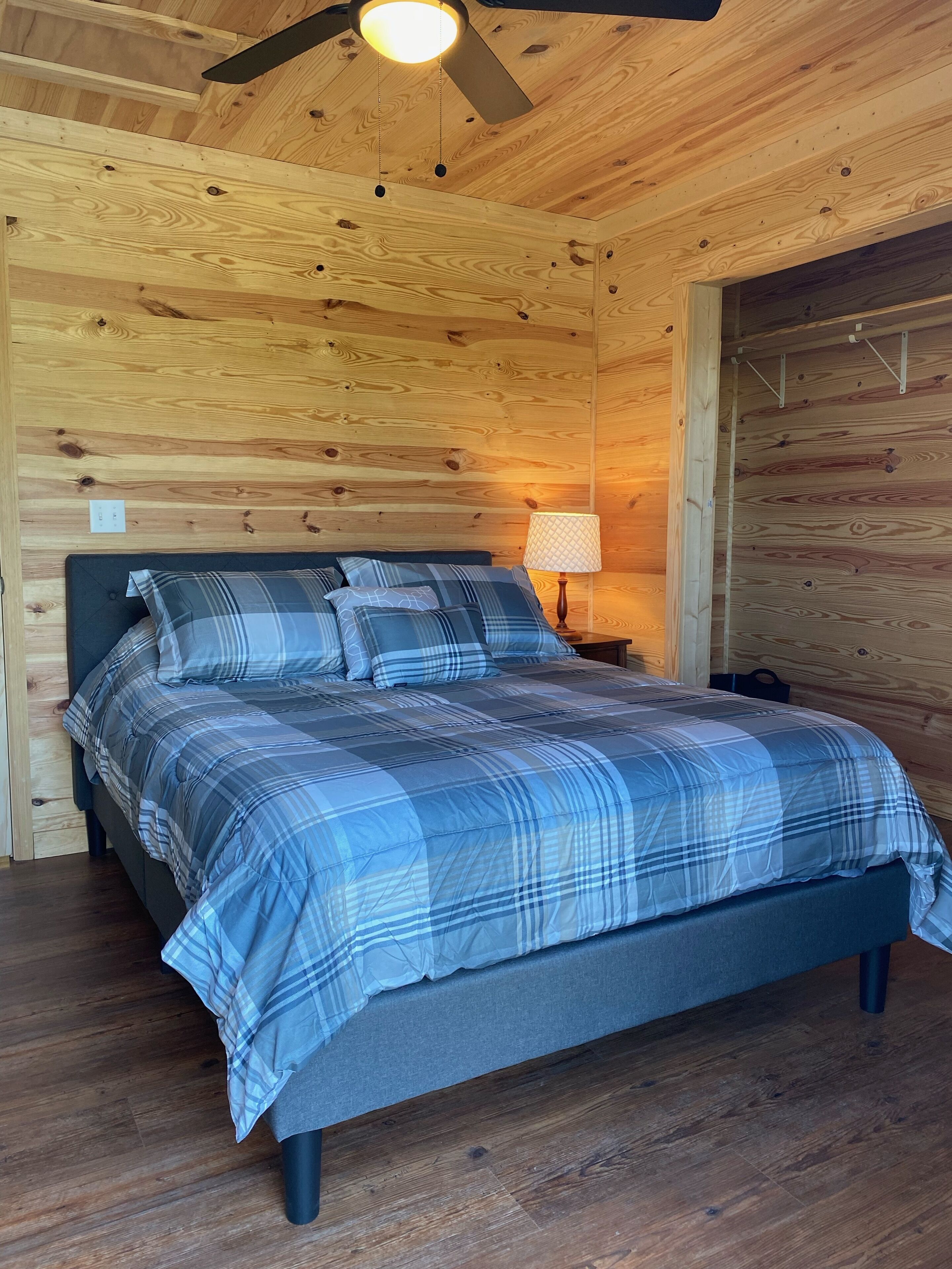 A wooden cabin bedroom with a bed, a nightstand, a lamp, and a ceiling fan.