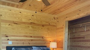A wooden cabin bedroom with a bed, a nightstand, a lamp, and a ceiling fan.